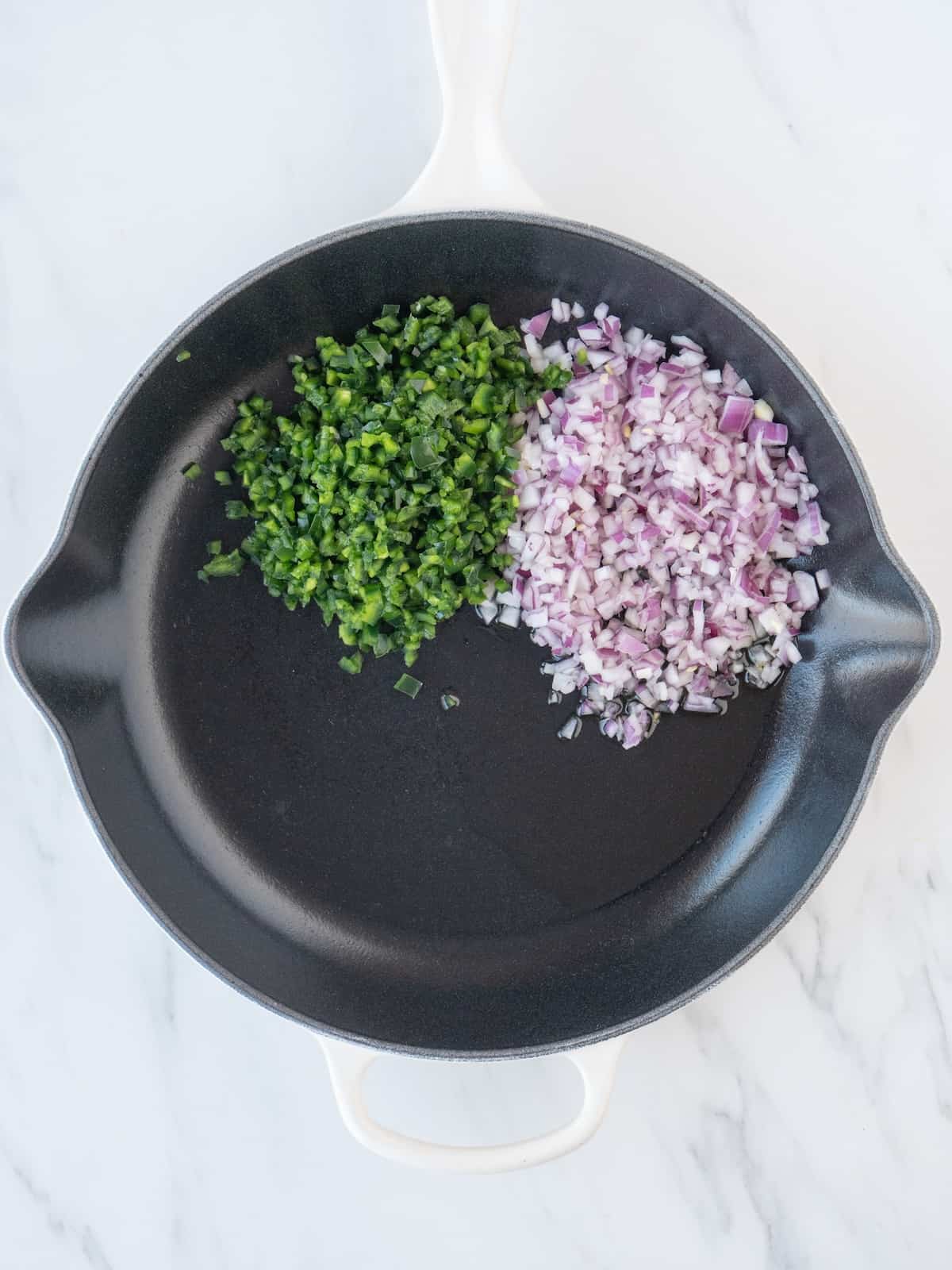 A skillet with finely chopped onion and poblano peppers being sautéed.