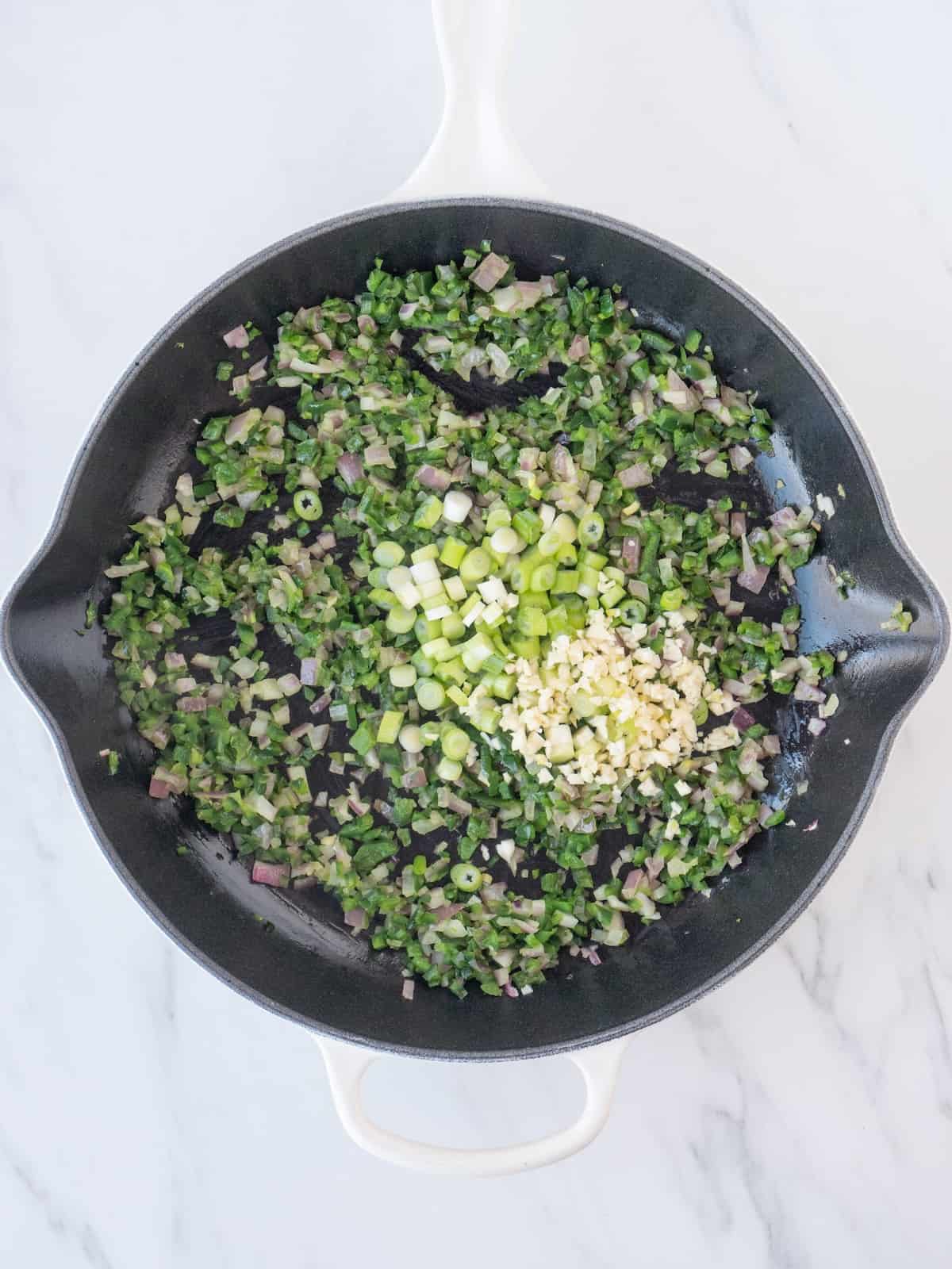 A skillet with sautéed finely chopped onion and poblano peppers, and chopped green onions and garlic just added.