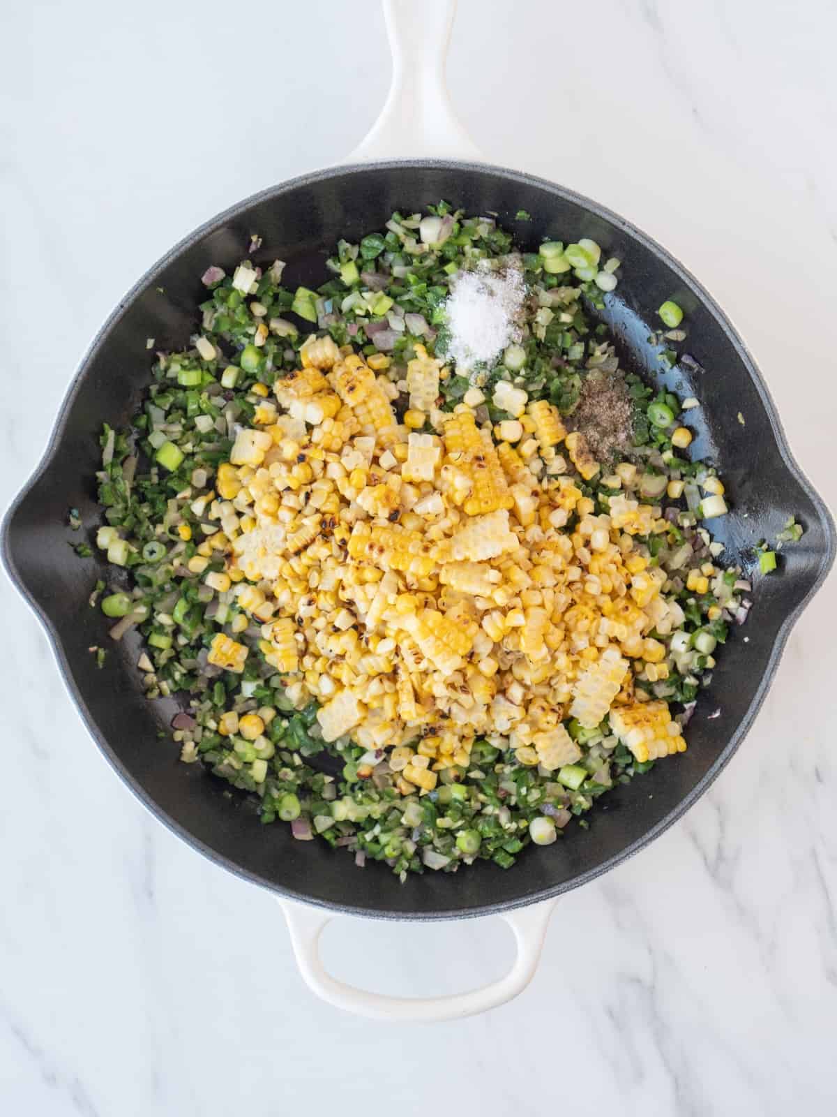 A skillet with sautéed onions and peppers to make avocado corn salad, and grilled corn just added.