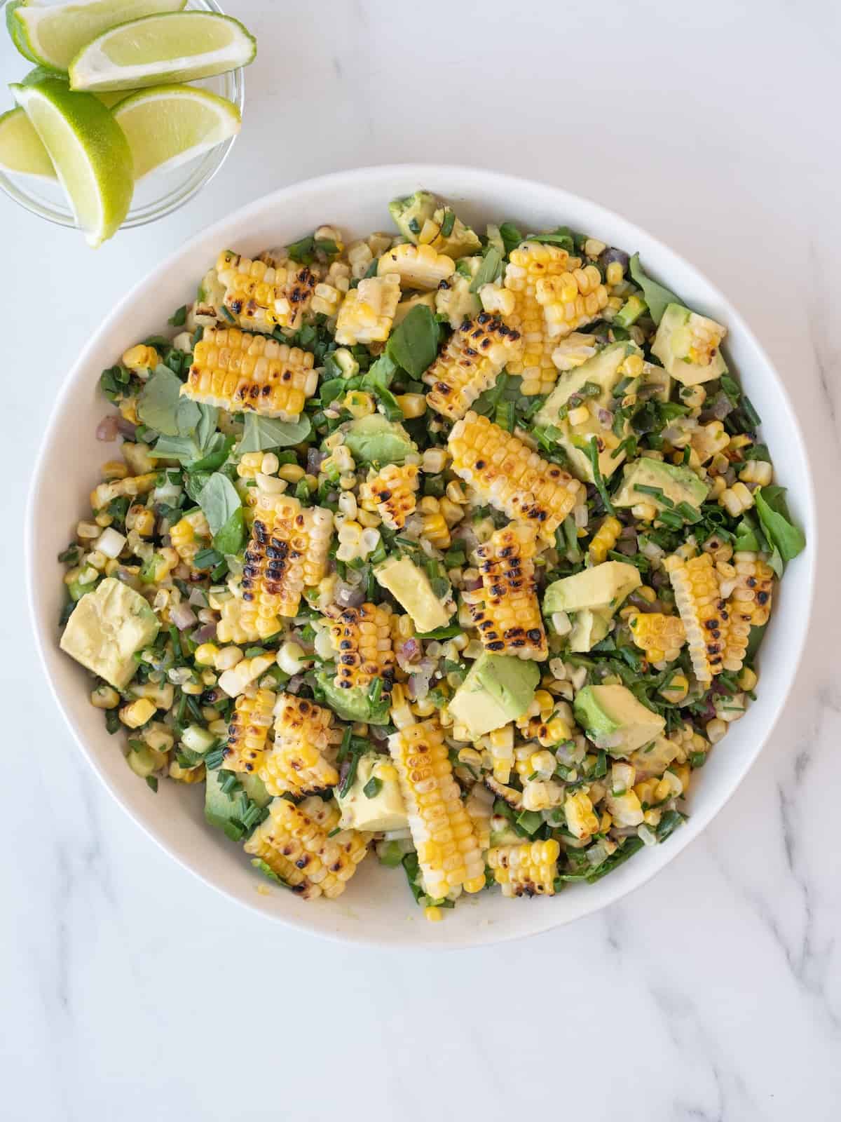 A bowl with avocado corn salad, and a small glass mixing bowl on the side with lime wedges.