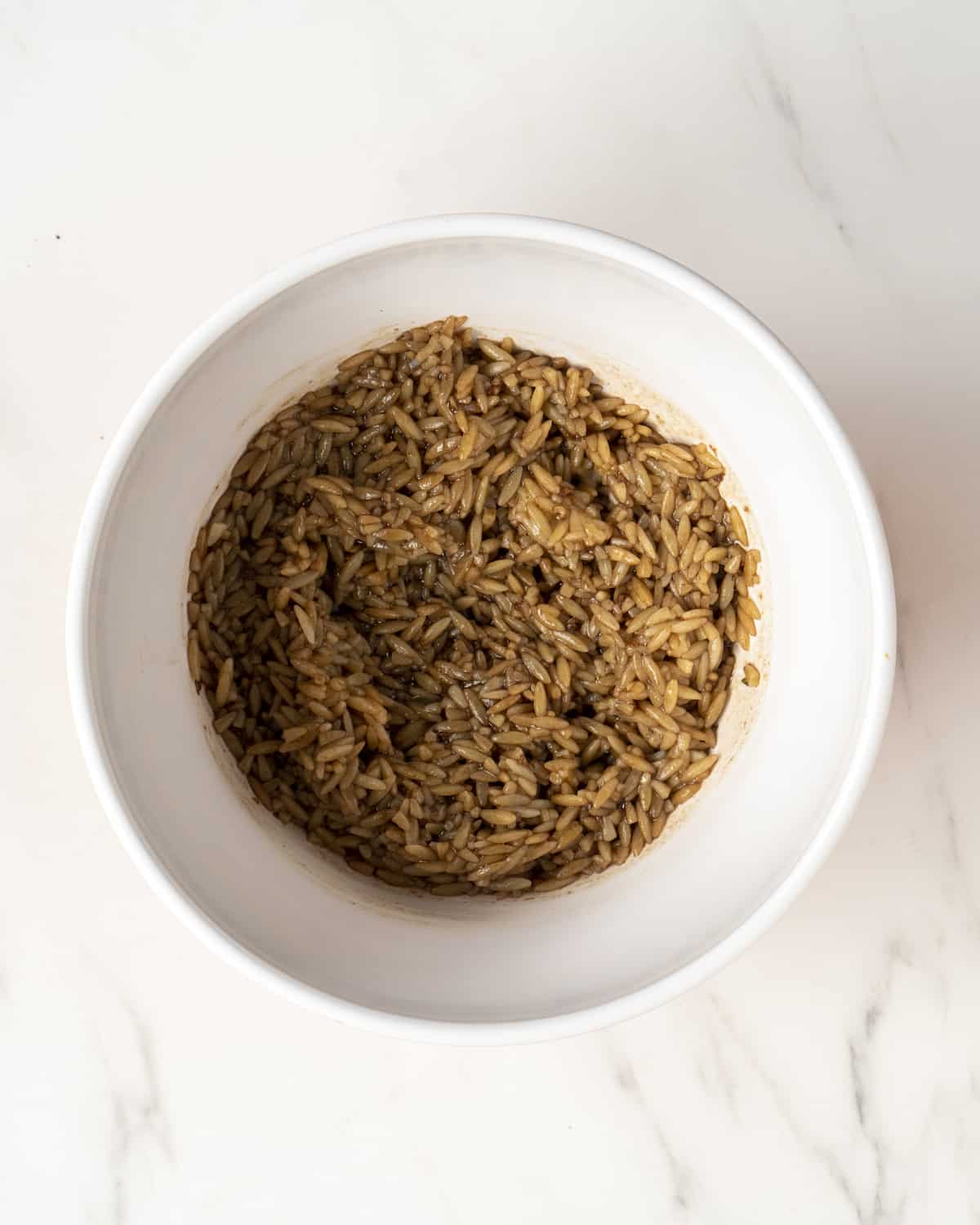 cooked orzo mixed into the balsamic dressing in a large white mixing bowl.