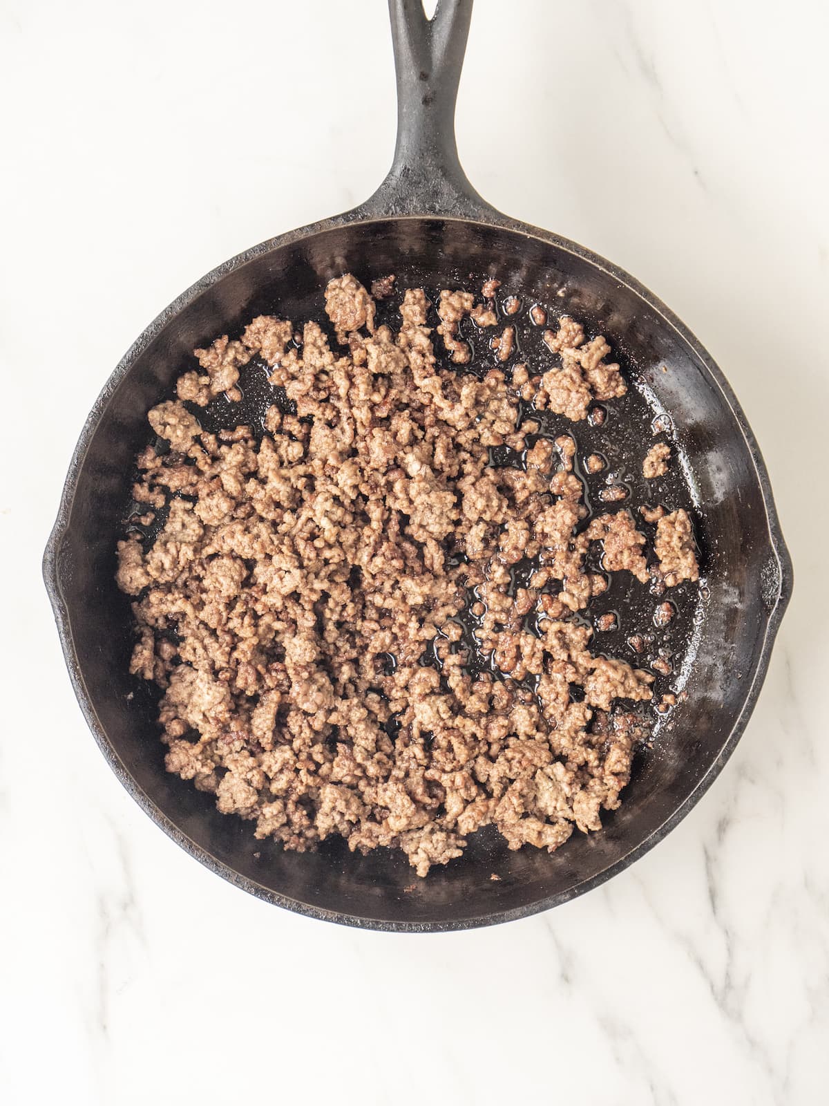 An 8" skillet with ground beef being cooked.