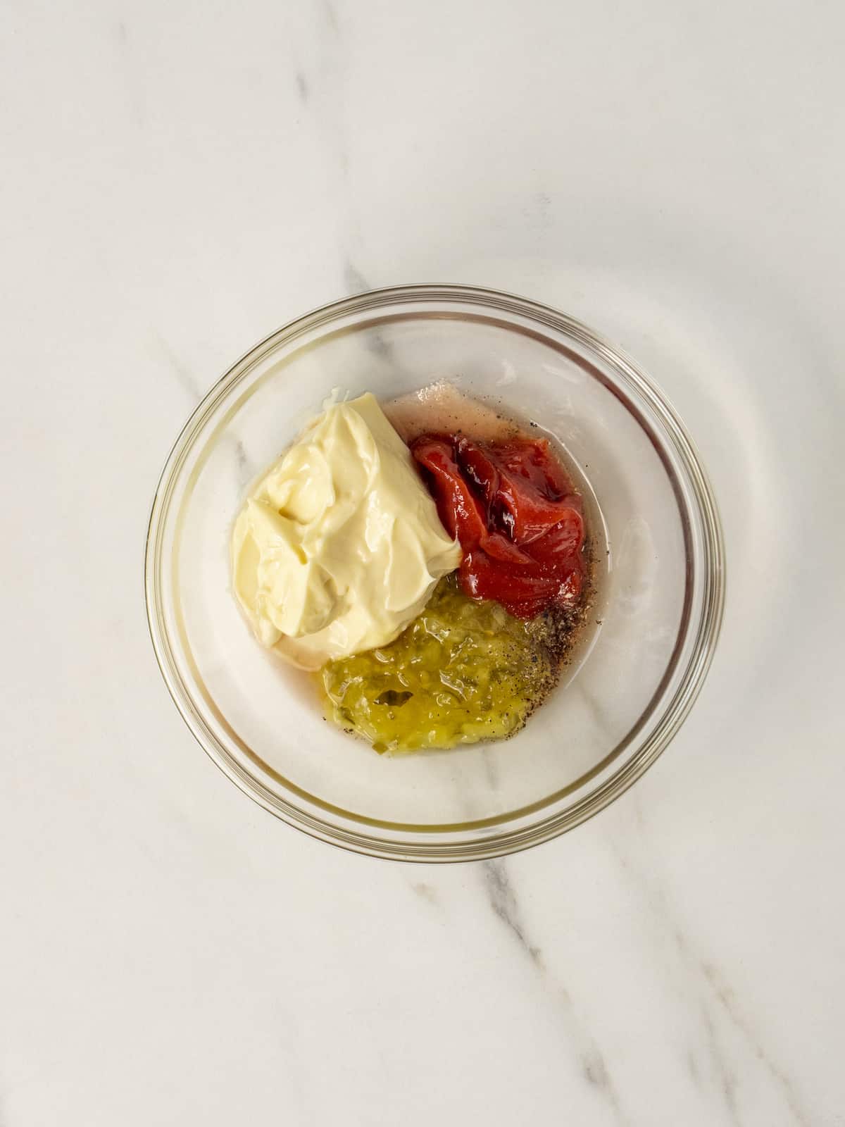 A small glass mixing bowl with mayonnaise, ketchup and sweet relish.