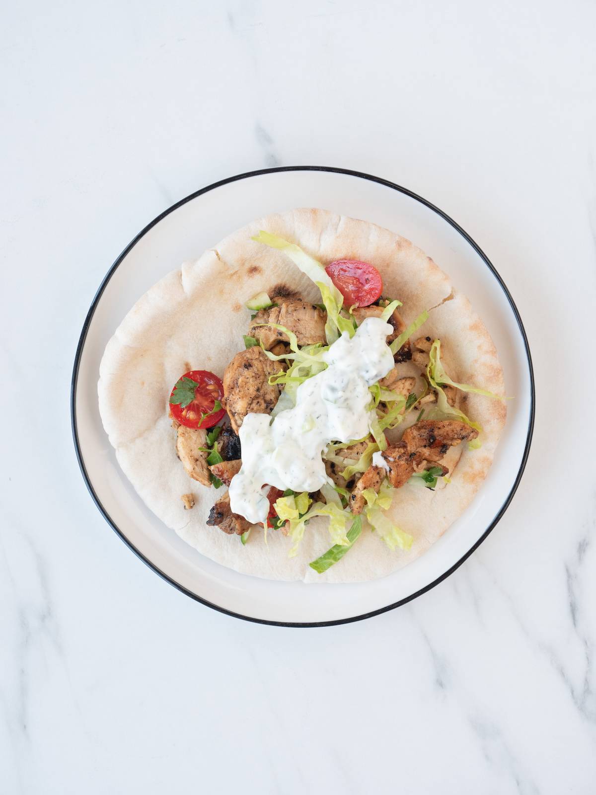 A white place with pita filled with a chicken, cucumber and tomato mixture, topped with shredded lettuce and tzatziki sauce.