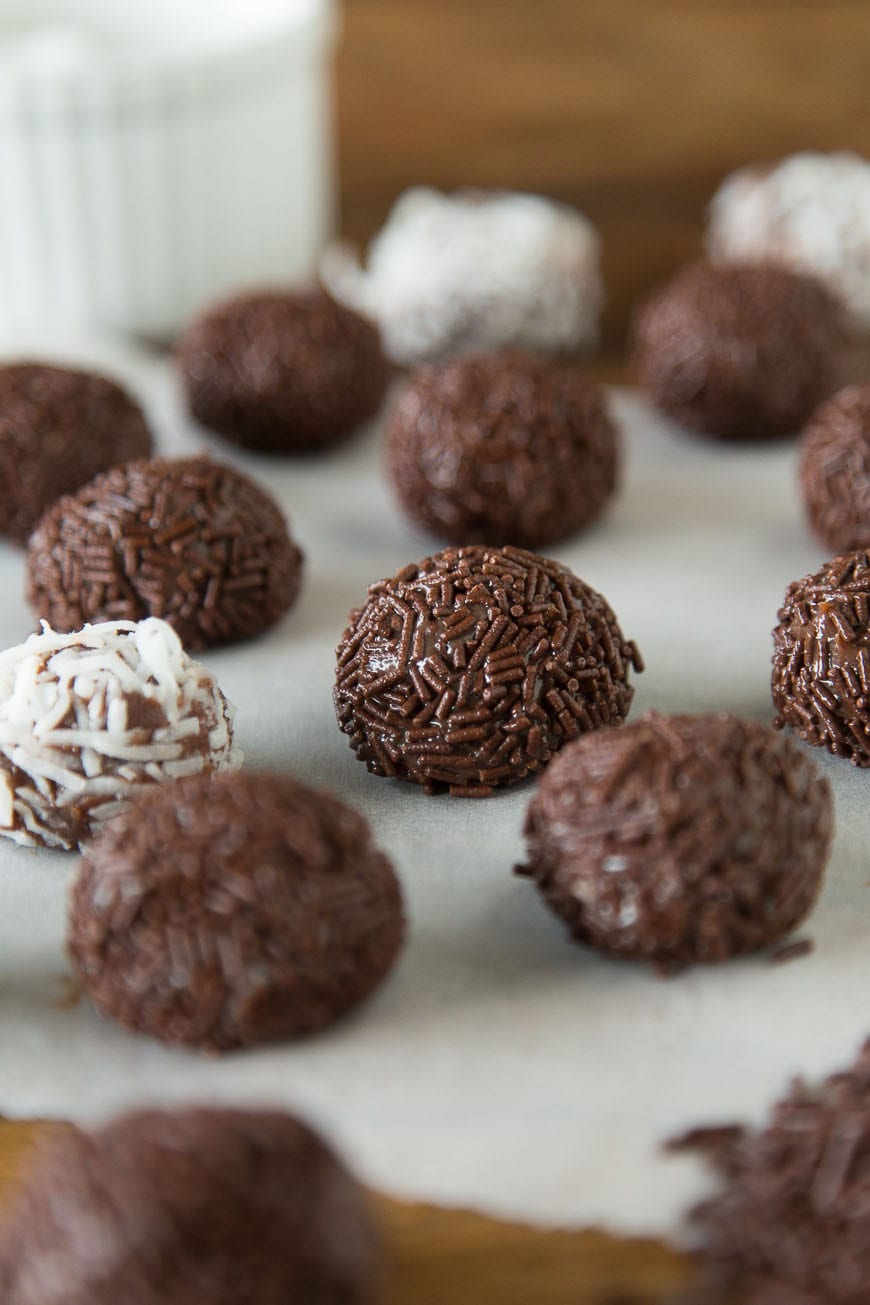 Brigadeiro - A Brazilian Chocolate Bonbon covered in chocolate sprinkles! A parchment-lined baking dish with Brigadeiro, some coated in chocolate sprinkles and some in coconut, with the background blurred out.