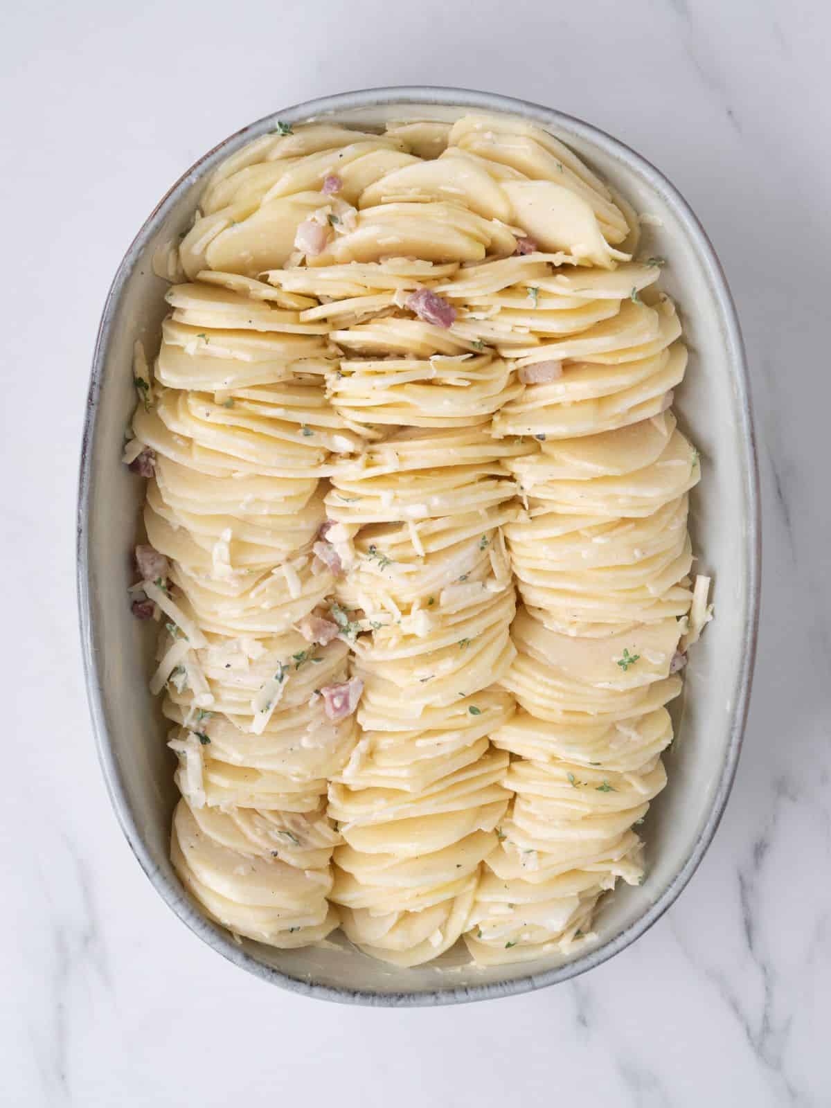 An oval baking dish with sliced potatoes dipped in cream mixture arranged in three columns.