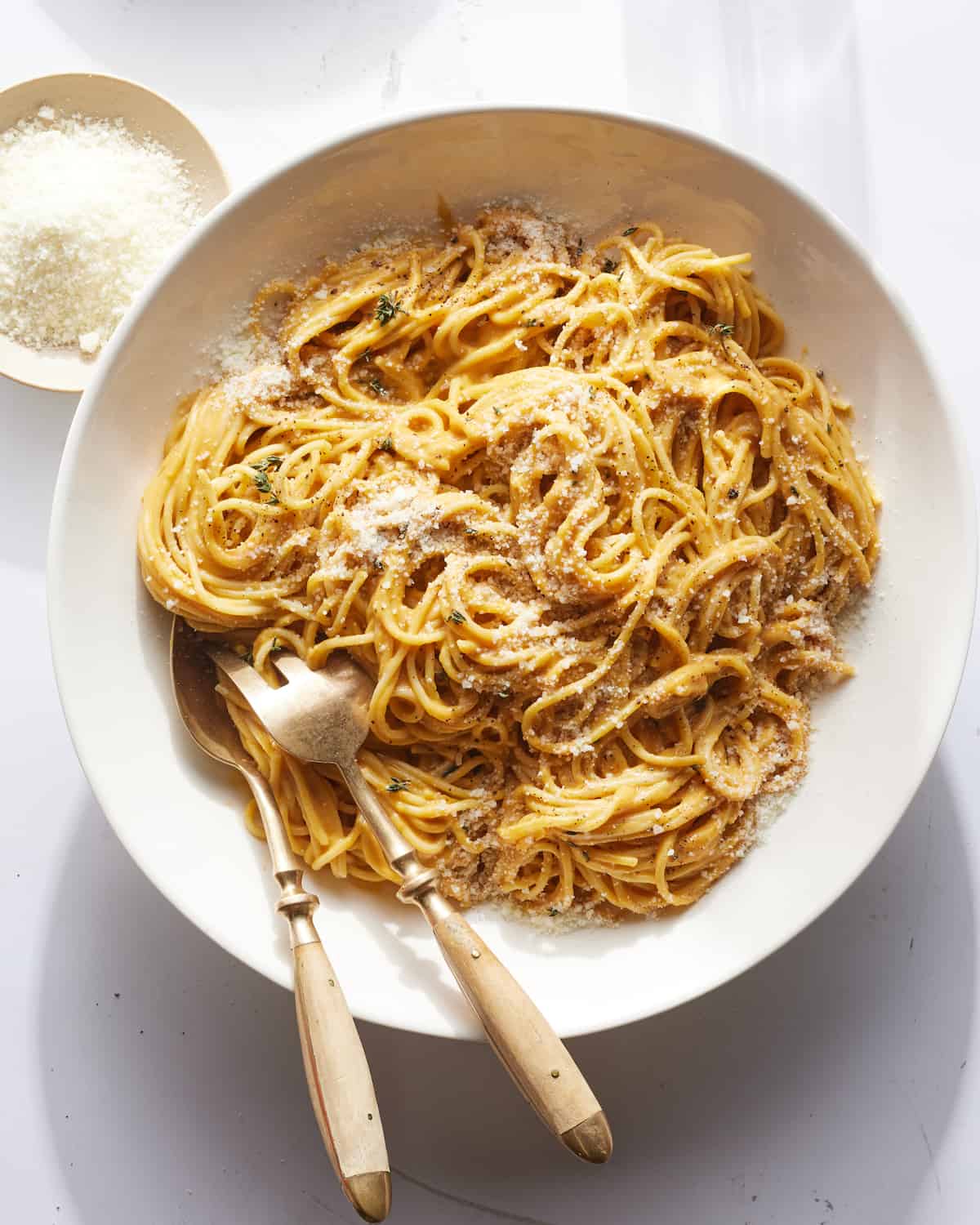 A large bowl full of butternut squash next to a small bowl of pecorino cheese.  