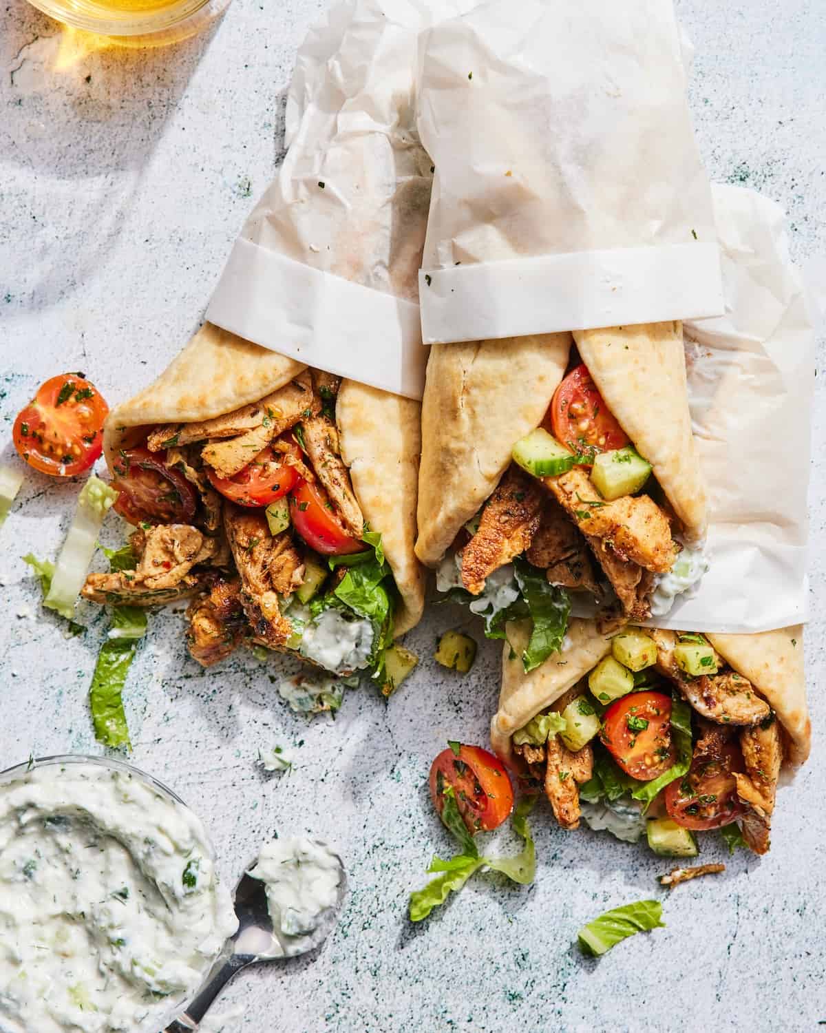 Chicken Gyros wrapped in parchment paper with a bowl of tzatziki on the side.