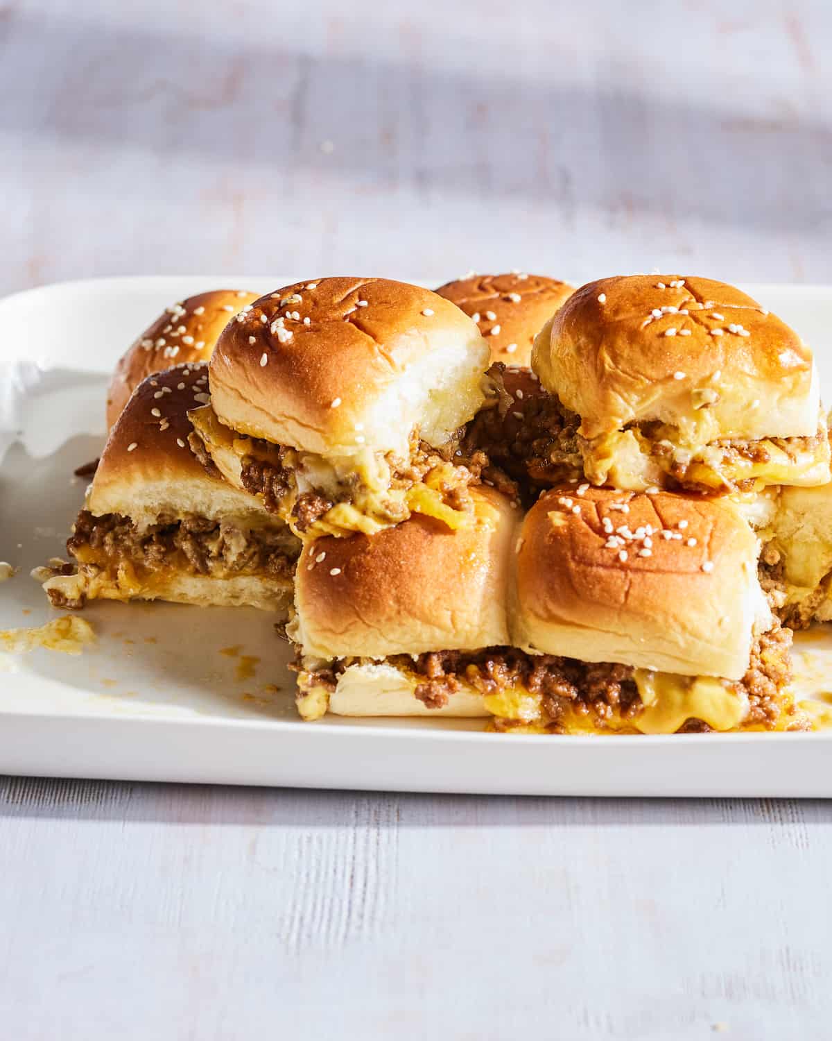 A white platter with about 8 cheeseburger sliders placed one on top of the other.