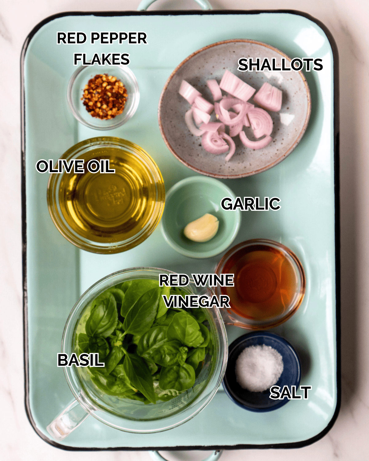 Basil Vinaigrette Ingredients: shallot, basil, garlic, red pepper flakes, olive oil, red wine vinegar, salt and pepper measured and prepped out on a blue enamel tray
